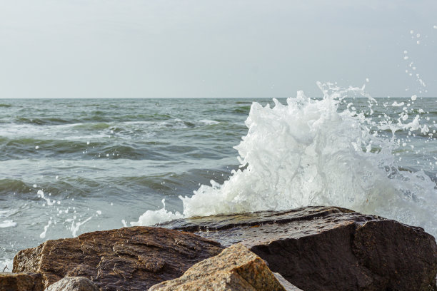 海浪的镜头。水花溅到石头上。海浪在岩石间翻腾。潮水的背景。图片下载