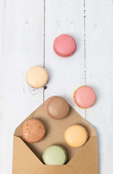 马卡龙从信封里掉出来，落在白色木桌上。图片下载