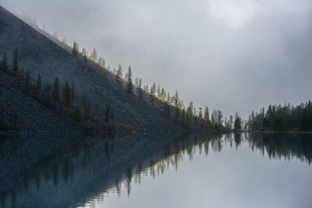 清晨，冰湖上的冷杉顶反射出宁静的朦胧景色。图形EQ云杉山顶在金色的阳光在神秘雾的高山湖泊。山湖。图片下载