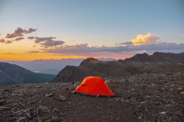 风景秀丽的高山景观，帐篷在非常高的海拔，在橙色的黎明天空中看到大山。生动的橙色帐篷，在多云的天空下，日落的颜色下，可以看到令人敬畏的高山。图片下载