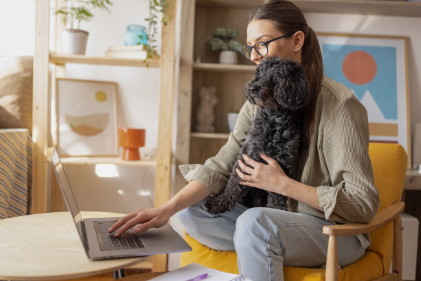 年轻漂亮的女人使用笔记本电脑，而她可爱的小狗坐在她的腿上图片下载