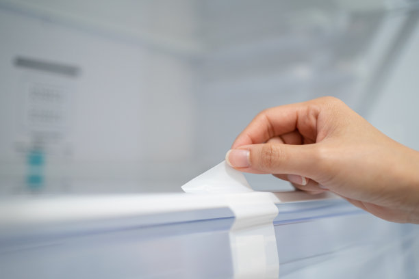 裁剪妇女的手拆除一个新冰箱的保护贴纸图片下载