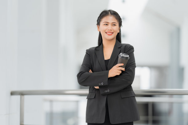 亚洲女商人站着的肖像，她穿着黑色西装，微笑着站在一个好心情。有一个复制空间和隔离。图片下载