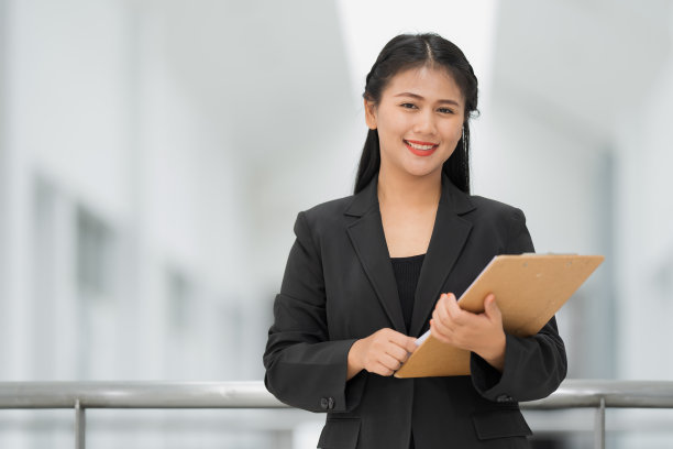 亚洲女商人站着的肖像，她穿着黑色西装，微笑着站在一个好心情。有一个复制空间和隔离。图片下载