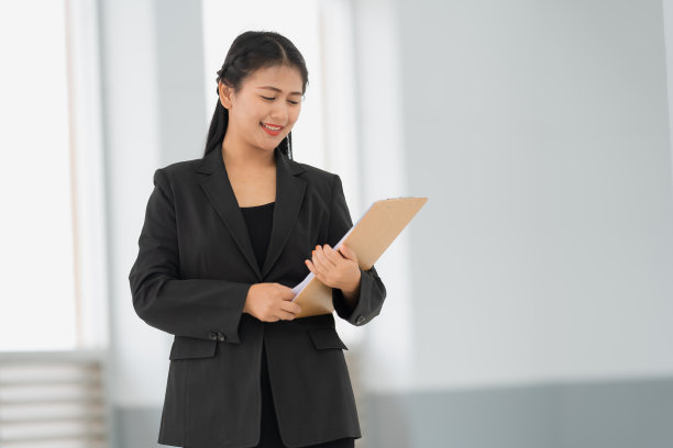 亚洲女商人站着的肖像，她穿着黑色西装，微笑着站在一个好心情。有一个复制空间和隔离。图片下载