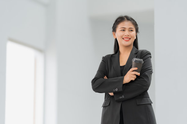 亚洲女商人站着的肖像，她穿着黑色西装，微笑着站在一个好心情。有一个复制空间和隔离。图片下载
