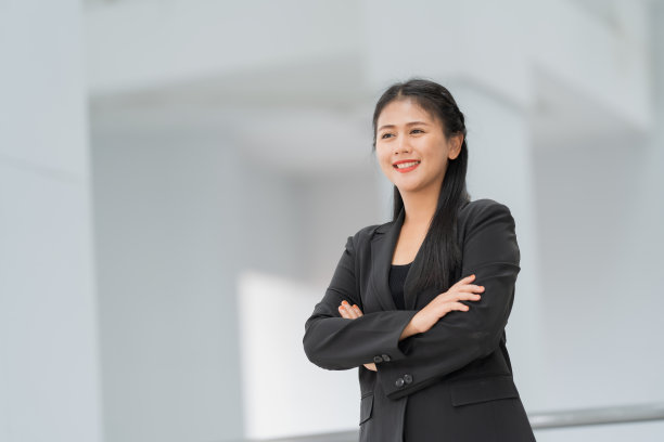 亚洲女商人站着的肖像，她穿着黑色西装，微笑着站在一个好心情。有一个复制空间和隔离。图片下载