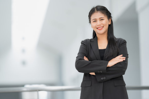 亚洲女商人站着的肖像，她穿着黑色西装，微笑着站在一个好心情。有一个复制空间和隔离。图片下载