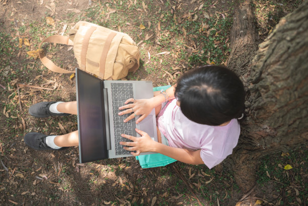 一名十几岁的女子在公园里用手机和笔记本电脑学习图片下载