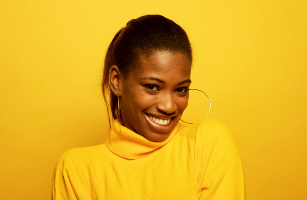 迷人的非洲裔美国妇女在黄色毛衣微笑快乐。肖像在黄色背景。图片下载