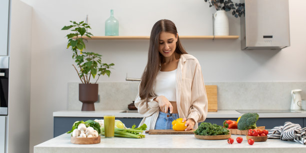 一位美女站在厨房的餐桌旁，切蔬菜做沙拉。健康饮食图片下载