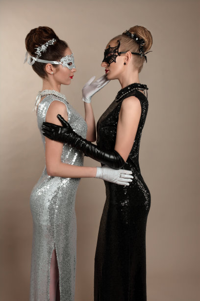 肖像的两个美丽的女人金发和黑发在别致的白色和黑色闪亮的连衣裙手套。化妆和发型，配饰和图片下载