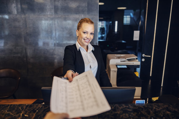 一位接待员站在接待处给顾客发文件。图片下载