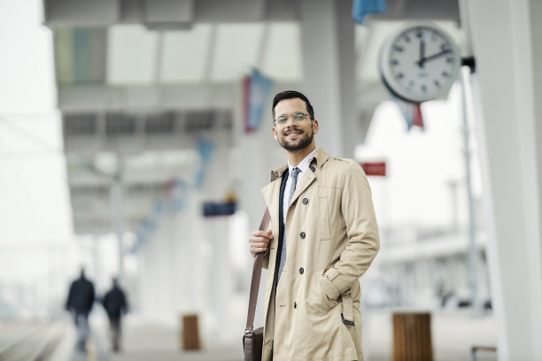 一个快乐的年轻人站在火车站等火车。图片下载