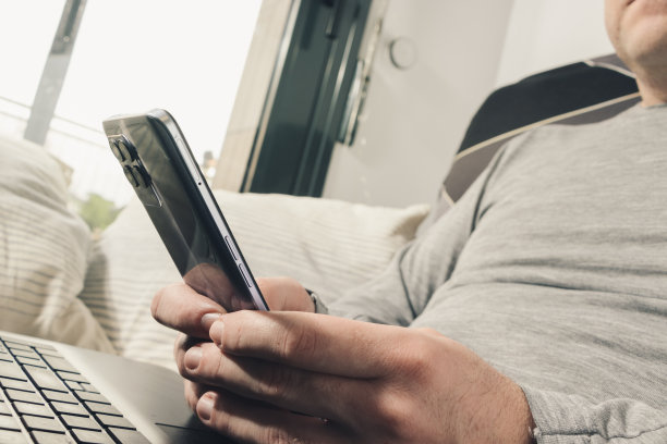 特写:双手拿着手机，膝上放着笔记本电脑图片下载