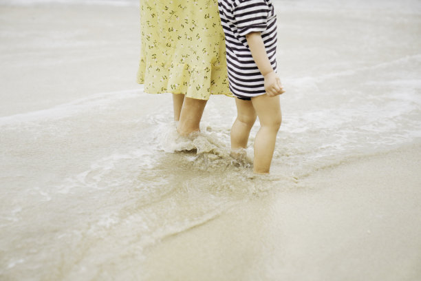 年轻的亚洲妇女在沙滩上教她的孩子走路图片下载