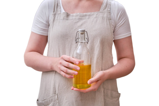 橄榄油玻璃瓶在厨房的女人旁边，孤立在白色背景上。女性手里拿着一瓶黄色的油图片下载