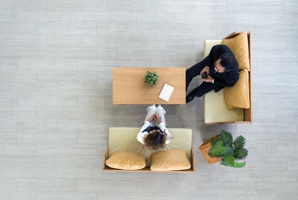 高视角的现代共享办公空间。年轻的亚洲女商人，穿着白色西装，手里拿着咖啡杯与高级经理交谈。花盆和笔记本在木桌上。图片下载