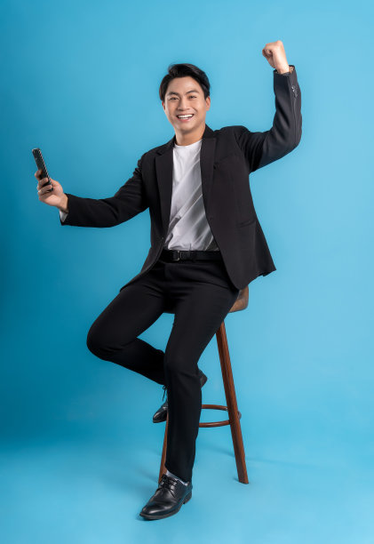 年轻的商人穿着背心使用手机，并在蓝色背景上摆姿势图片下载