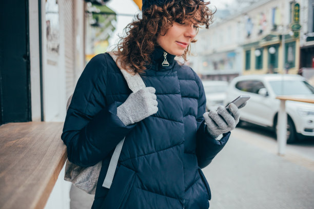 冬天的一天，年轻女子站在城市街道上使用手机图片下载