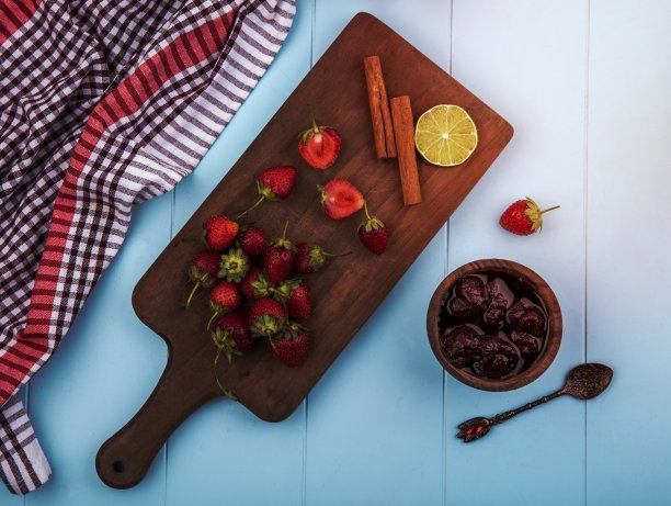俯视图新鲜草莓在木制厨房板与肉桂棒草莓果酱在蓝色背景图片下载