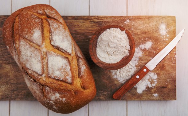 顶部视图的硬皮面包与一碗面粉和刀在砧板上的木制背景图片下载