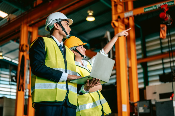 工厂经理和戴安全帽的工人使用笔记本电脑和公司应用程序讨论检查结果。制造业团队合作理念。图片下载