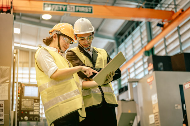 男女工业工程师戴着安全帽在工业制造工厂讨论新项目，同时使用蓝图。工程师和建筑师的概念。图片下载
