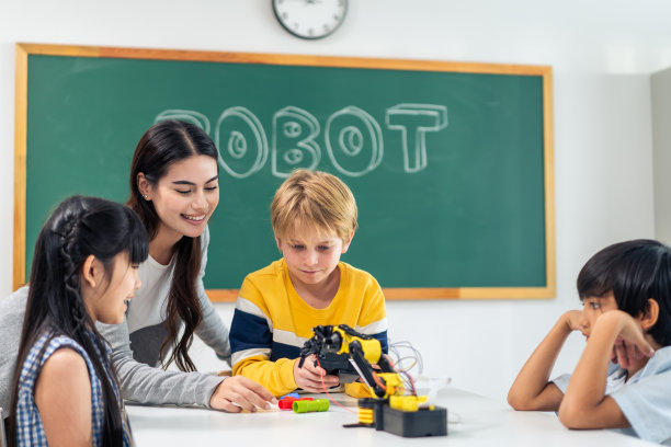 一群小学生在教室里跟着老师学习。迷人美丽的女指导老师在幼儿园用快乐有趣的活动为幼儿讲解和教育。图片下载