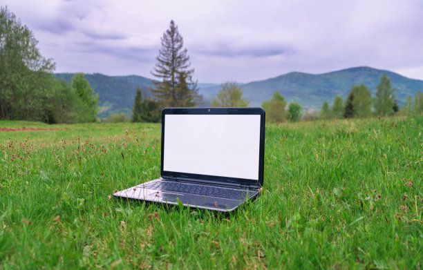 笔记本电脑，绿色草坪上的空白屏幕，背景是山脉。下载图片图片下载