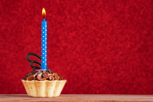 生日小蛋糕，红色背景，复制空间。焦糖小蛋糕配一支蓝色蜡烛图片下载