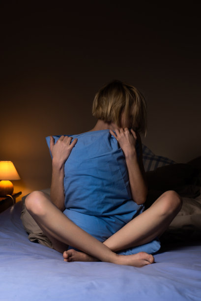 一个女人在黑暗的房间里抱着一个枕头。孤独，睡眠准备，睡眠障碍，昼夜节律概念。图片下载