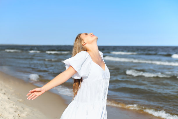 幸福的微笑着美丽的女人在沙滩上穿着白色的夏装，张开双臂图片下载
