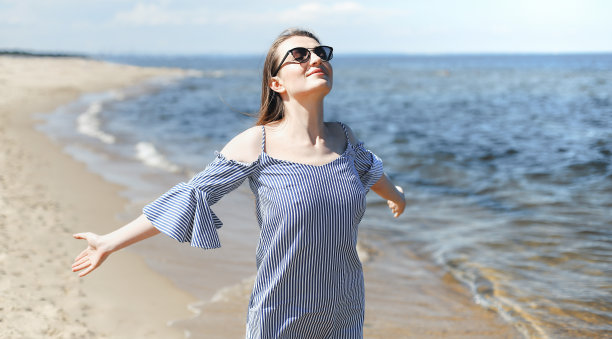 快乐的微笑女人在自由的幸福在海滩上站着张开双手。肖像的黑发女模特在夏季连衣裙享受自然旅行假期假期户外图片下载