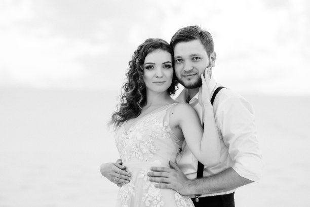 一对年轻的夫妇，一个穿黑色马裤的男人和一个穿粉红色裙子的女孩在白色的沙滩上散步图片下载