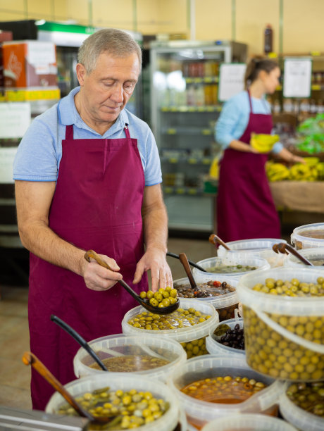 熟练成熟的男性超市工人，穿着围裙，在超市出售各种橄榄和泡菜图片下载