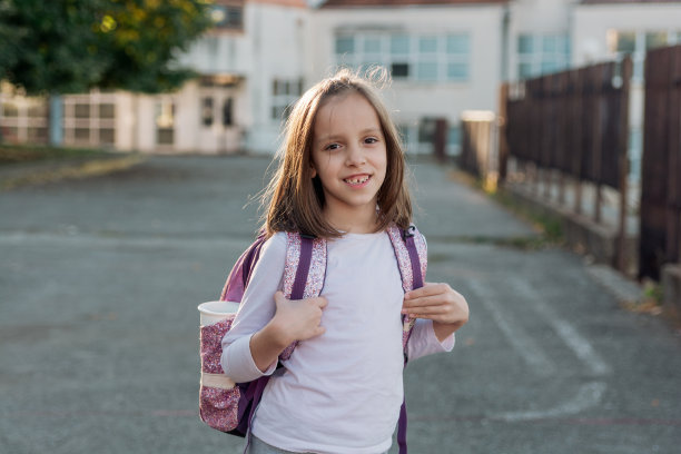 微笑的小学女孩背着背包站在学校前面的肖像图片下载