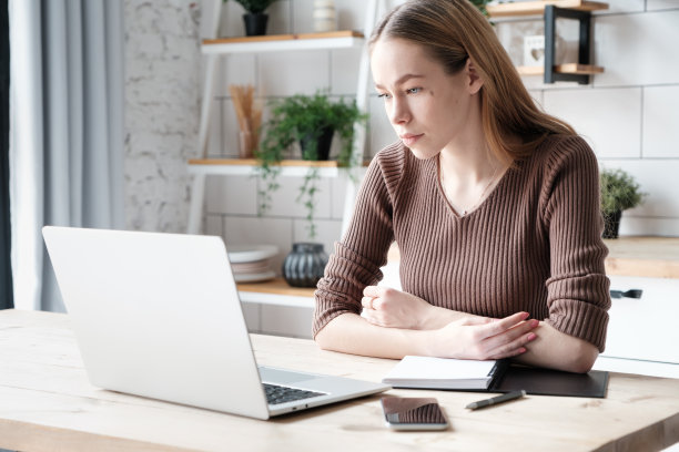 有思想的白人年轻女性远程工作者，有笔记本电脑，智能手机，记事本图片下载