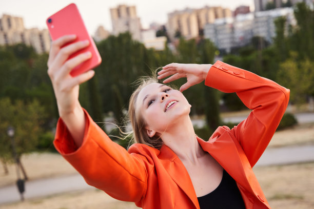 穿着休闲装的漂亮微笑模特。性感无忧无虑的女性在街上摆姿势。智能手机自拍自拍照片图片下载
