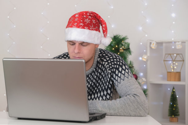 戴圣诞帽的男子在新年假期用笔记本电脑网购。一名男子用笔记本电脑订购圣诞礼物，并用信用卡支付。那个男人手里拿着一张信用卡。图片下载