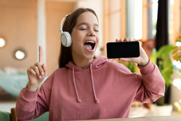 欣喜若狂的少女在手机上唱歌，听音乐，戴着无线耳机，在家里玩得很开心图片下载