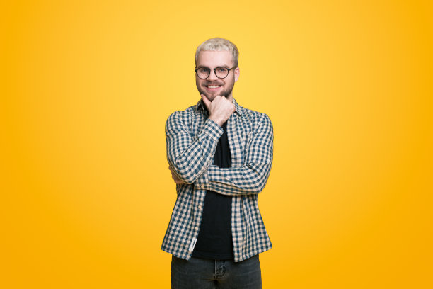 满意的白人男子胡须肖像，他的手在他的下巴微笑与自鸣得意的脸，戴眼镜，站在黄色背景图片下载