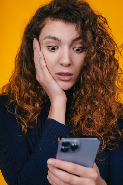 惊讶地盯着智能手机的女子收到通知，大眼睛被黄色背景隔离。在线交流。孤立的女性肖像。图片下载