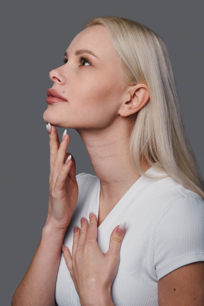 一个美丽的女人触摸柔软光滑的皮肤颈部站在灰色的背景。享受她的美丽。面部护肤品。卫生保健。身体保健。图片下载