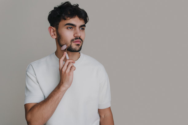 男子使用玉面辊为皮肤护理隔离在灰色背景与复制空间。面部皮肤护理。完美的美容护肤。图片下载