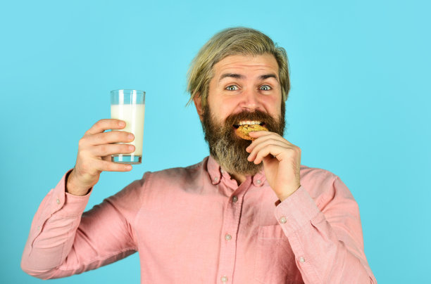 有机农产品早餐或午餐。牛奶和饼干。快乐的农民吃饼干甜点。大胡子男人喝有用的牛奶和糕点。健康饮食的概念图片下载