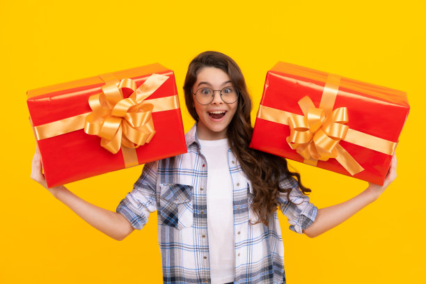在黄色背景下，拿着礼物的惊讶的青少年儿童。戴眼镜的青少年儿童图片下载