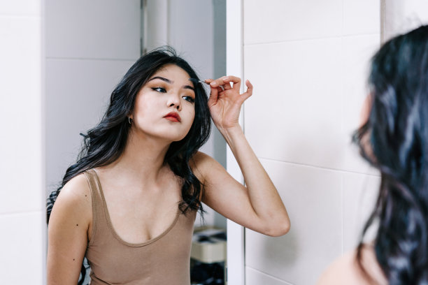 头部特写微笑的亚洲年轻女子使用化妆品刷，看着镜子，美丽的女孩把日常化妆，应用粉末，淋浴后站在浴室图片下载