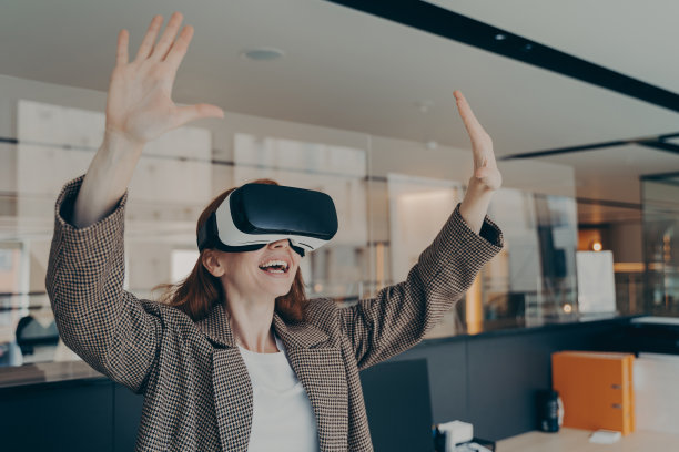 年轻兴奋的红发女商人正装坐在办公室内部使用VR耳机图片下载