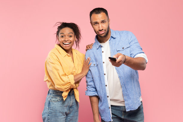 黑色情侣用遥控器在粉色演播室背景下观看电视节目或电视节目图片下载